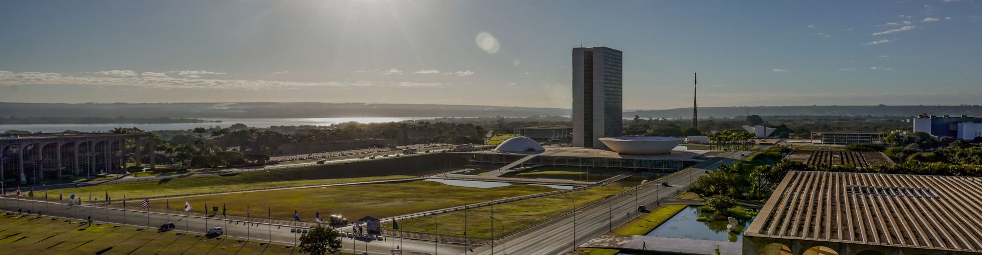 Vista panorâmica em ângulo elevado da Esplanada dos Ministérios em Brasília, sob luz solar intensa e um céu claro.