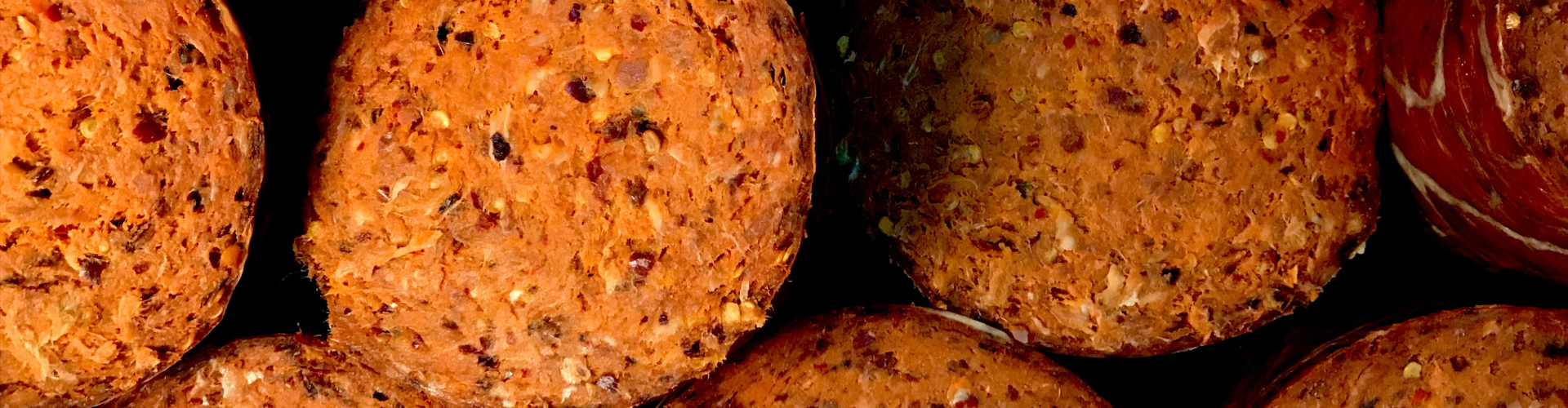 Fatias de 'nduja de porco preto, um embutido de cor alaranjada e textura rústica com especiarias visíveis