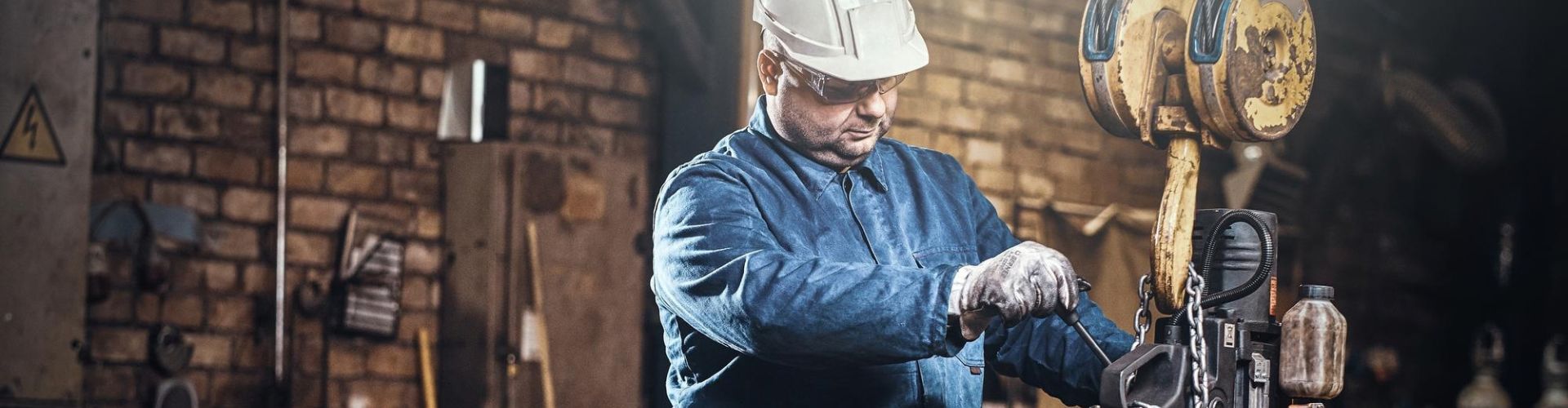 Trabalhador industrial de capacete e óculos operando maquinário pesado com gancho de elevação em oficina