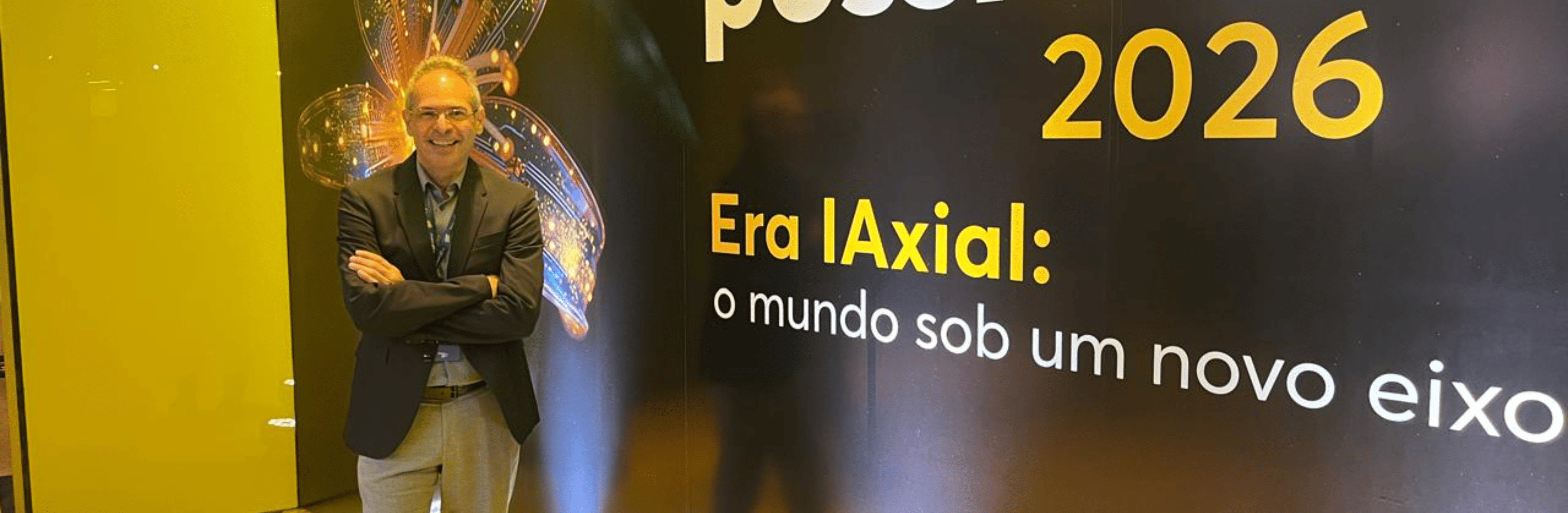 Homem sorridente de óculos e fato diante do painel do Festival Futuros Possíveis 2026 da Firjan
