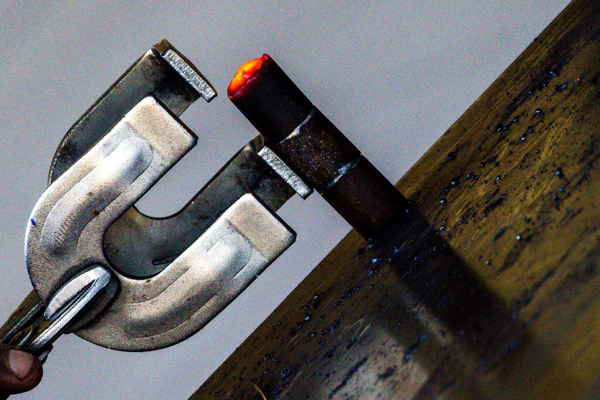 Alicate de pressão a fixar uma peça de metal com ponta incandescente sobre uma barra metálica