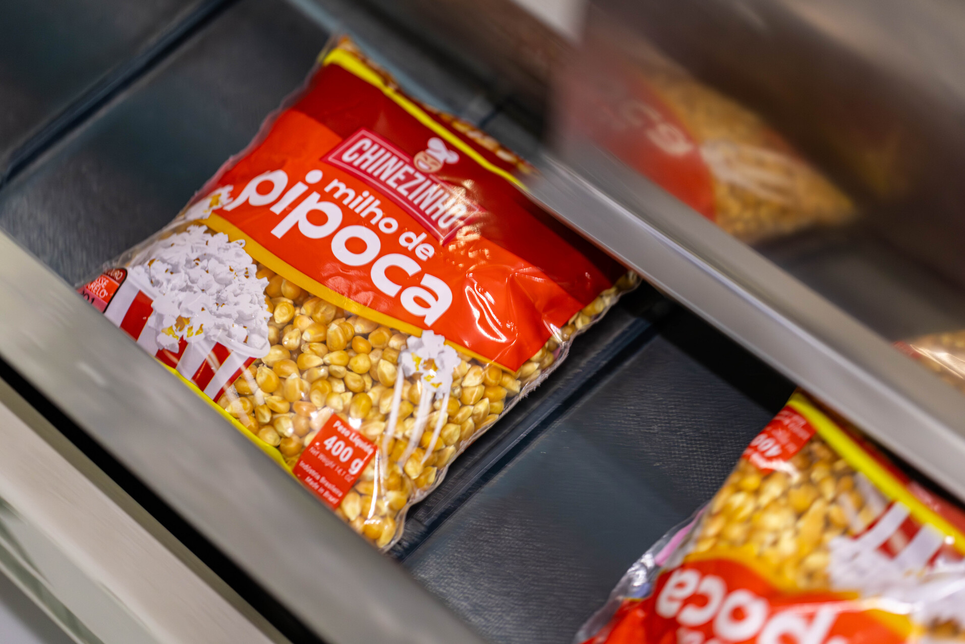 Pacotes de milho de pipoca da marca Chinezinho avançam numa esteira rolante automatizada.